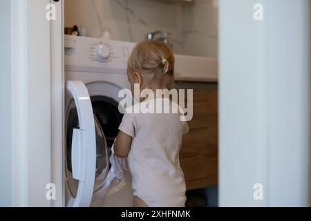 Zwei Jahre altes Kind, das Hausaufgaben macht. Waschmaschine wird geladen. Stockfoto