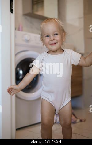 Zwei Jahre altes Kind, das Hausaufgaben macht. Waschmaschine wird geladen. Stockfoto
