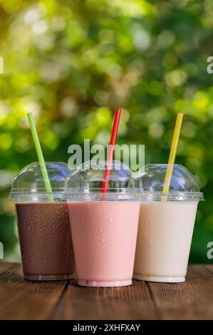 Set aus verschiedenen leckeren Milchshakes in Einweg-Plastikgläsern mit Stroh auf dem Tisch draußen Stockfoto