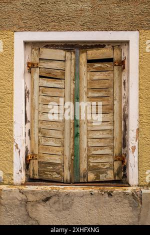 Weiße alte Holzfenster mit grauen Fensterläden an der gelben Hausfassade Stockfoto