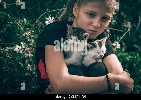 Blondes Mädchen, das kleine, entzückende Katzen im Garten hält Stockfoto