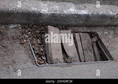 Der alte Sturmabfluss ist mit Brettern und Blättern des letzten Jahres verstopft Stockfoto