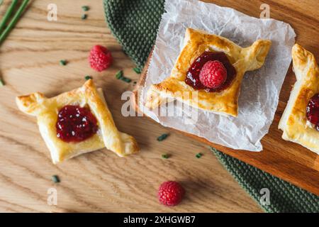 Köstliches Blätterteiggebäck gefüllt mit Camembertkäse und Himbeermarmelade, serviert auf einem Holzbrett mit frischen Himbeeren. Essen von oben für Stockfoto