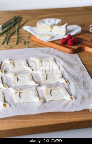 Zubereitung von Blätterteigscheiben mit Camembertkäse und frischen Himbeeren auf einem Holztisch. Stockfoto