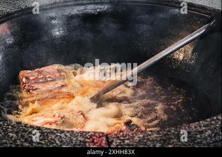 In der Küche eines Restaurants in Usbekistan kocht der Küchenchef Lammfleisch in einem kochenden Kessel für traditionelles orientalisches usbekisches Pilaw Stockfoto