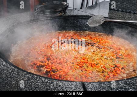 Karotten, Kichererbsen und Rosinen werden in einem Kessel gekocht, um traditionelle orientalische usbekische Pilaw in der Küche eines Restaurants in Usbekistan zu kochen Stockfoto