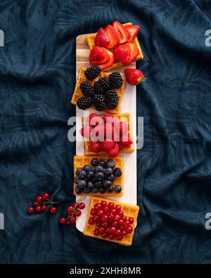 Waffeln mit frischen Sommerbeeren auf dunklem blauem Blumenhintergrund Stockfoto