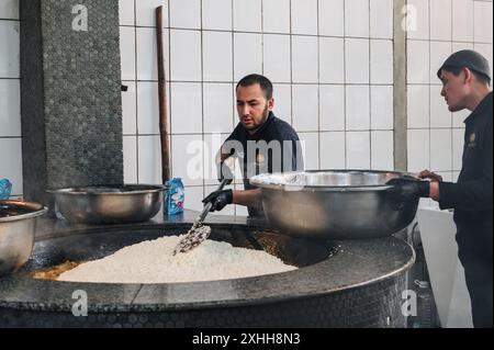 Männliche Köche bereiten Reis für usbekische Pilaw in einem Kessel in der Küche eines Restaurants Central Asian Pilaf Center Besh Qozon zu. Taschkent, Usbekistan - 16. April 2024 Stockfoto