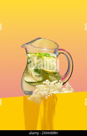 Hausgemachte frische Holunderblüten-Limonade, garniert mit Zitronenschale und einem blühenden Zweig auf einem hellrosa und gelben Hintergrund Stockfoto