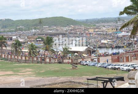 Blick auf die Goldküste von Cape Coast Castle, Cape Coast, Ghana - Fischerboote; Fischerhafen; Hafen; Boote; Menschen; Häuser; Palmen; Stockfoto