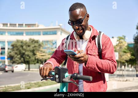 Glücklicher junger afrikanischer Mann, der mit dem Telefon einen Elektroroller fährt. Stockfoto