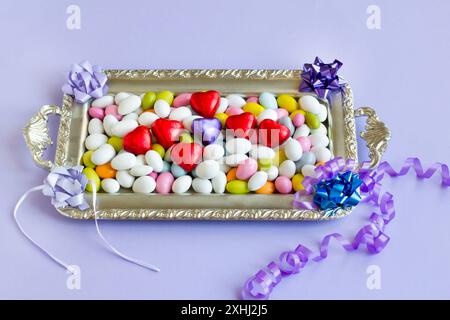 Farbenfrohe Mandelbonbons wurden auf silbernem Tablett mit herzförmigen gewickelten Pralinen gestaltet. Stockfoto