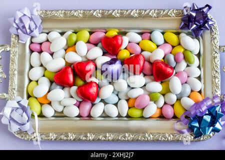 Farbenfrohe Mandelbonbons wurden auf silbernem Tablett mit herzförmigen gewickelten Pralinen gestaltet. Stockfoto