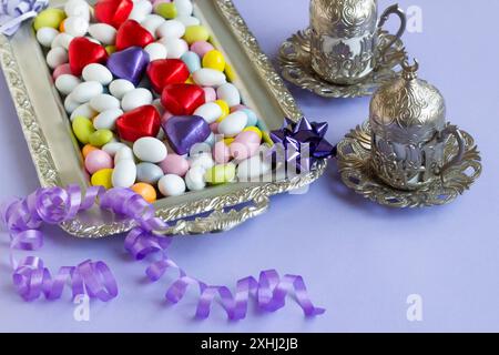 Farbenfrohe Mandelbonbons wurden auf einem silbernen Tablett mit herzförmigen gewickelten Pralinen und Kaffee entworfen Stockfoto