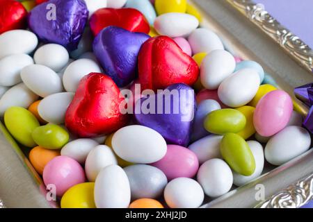 Farbenfrohe Mandelbonbons wurden auf silbernem Tablett mit herzförmigen gewickelten Pralinen gestaltet. Stockfoto