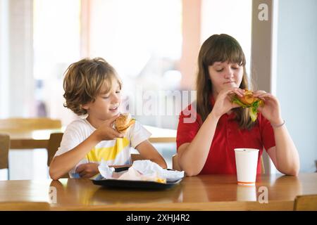 Kinder essen Fastfood. Ungesundes Junk Food. Kinder essen Burger, Chips und Chicken Nuggets im Fast Food Café. Junge und Mädchen essen zu Mittag. Schneller Snack Stockfoto