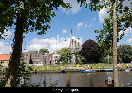 Boote parkten am niederländischen Ufer des Flusses Hollandse Ijssel zwischen Altstadt und Goudasfalt. Häuser auf der Straße neben 't Slot Windmühle. Stockfoto