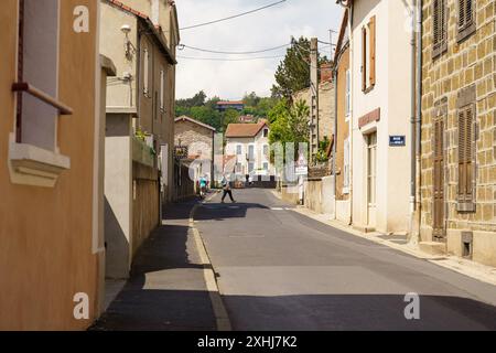 Langeac, Frankreich - 28. Mai 2023: Eine Einzelperson geht eine ruhige Straße in Langeac, Frankreich, entlang, umgeben von alten Steinhäusern und üppigem Grün. Stockfoto