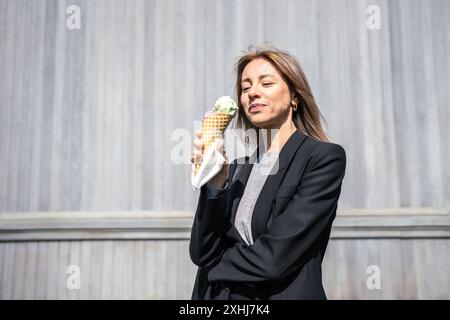 Lächelnde Frau genießt Eis in Kegel, fröhlich baden in Sonnenstrahlen im Sommer. Stockfoto