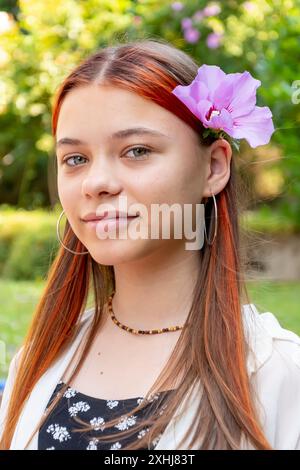 Porträt eines schönen 13-jährigen Mädchens im Teenageralter mit einer Blume im Haar vor dem Hintergrund eines blühenden Gartens. Stockfoto