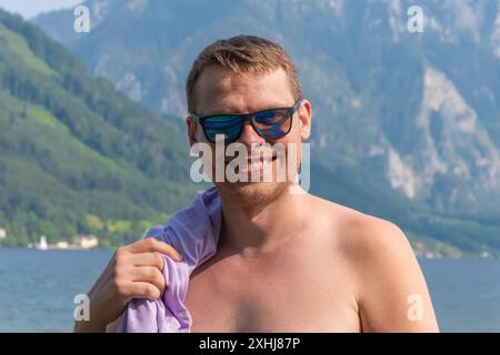Porträt eines 40-45-jährigen Mannes in Sonnenbrille auf dem Hintergrund von Bergen und Wasser. Stockfoto