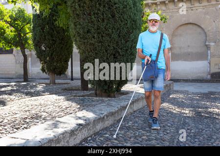 Ein reifer blinder Mann führt sich mit einem weißen Stock durch einen historischen Park. Vorderansicht. Stockfoto