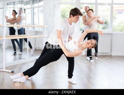 Fleißige, moderne Balletttänzer üben Ballettpositionen mit Unterstützung im Saal mit Ballettbar Stockfoto