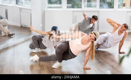 Mädchen und ihre Schüler führen Hip-Hop-Tanz auf einem gebogenen Bein auf, Bewegung in horizontaler Ebene in Bodennähe Stockfoto