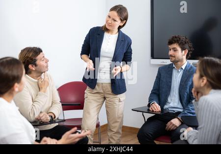 Positiv erfolgreiche Lehrerin, die Antworten von Schülern unterschiedlichen Alters hört, während sie im Kreis beim Fremdsprachenunterricht sitzt Stockfoto