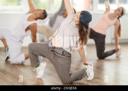 Mädchen und ihre Schüler führen Hip-Hop-Tanz auf einem gebogenen Bein auf, Bewegung in horizontaler Ebene in Bodennähe Stockfoto