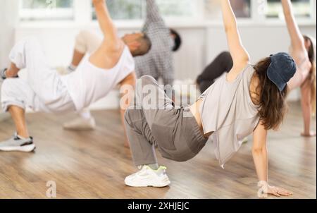 Mädchen und ihre Schüler führen Hip-Hop-Tanz auf einem gebogenen Bein auf, Bewegung in horizontaler Ebene in Bodennähe Stockfoto