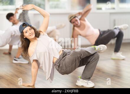 Mädchen und ihre Schüler führen Hip-Hop-Tanz auf einem gebogenen Bein auf, Bewegung in horizontaler Ebene in Bodennähe Stockfoto