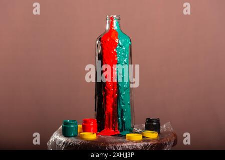 Geschlossenes Porträt einer Glasflasche mit Töpfen mit Farben in weiß, schwarz, gelb, grün, blau und rot. Abstrakt. Isoliert auf braunem Hintergrund. Stockfoto