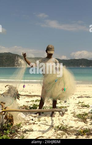 Ein Subsistenzfischer, der sein Fischernetz am Strand von Tarimbang in Tabung, East Sumba, East Nusa Tenggara, Indonesien, abrollt. Stockfoto