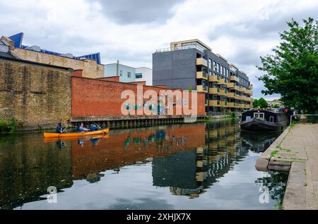 Damen im Kanu paddeln an einem Lastkahn vorbei, der vor dem Ufer des Grand Union Canal Paddington Arm in London liegt Stockfoto