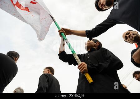 Srinagar, Indien. Juli 2024. Ein kaschmirischer schiitischer muslimischer Junge schwingt während einer Trauerprozession am siebten Tag Muharrams eine religiöse Flagge. Muharram ist der erste Monat des islamischen Kalenders. Es ist einer der heiligsten Monate im islamischen Kalender. Schiitische Muslime gedenken Muharram als einen Monat der Trauer zum Gedenken an das Martyrium des islamischen Propheten Muhammads Enkel Imam Hussain, der in der Schlacht von Karbala 680 n. Chr. auf Ashura (10. Tag Muharram) zum Märtyrertod verurteilt wurde. Credit: SOPA Images Limited/Alamy Live News Stockfoto