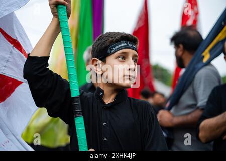 Srinagar, Indien. Juli 2024. Ein kaschmirischer schiitischer Junge hält eine religiöse Flagge während einer Trauerprozession am siebten Tag von Muharram. Muharram ist der erste Monat des islamischen Kalenders. Es ist einer der heiligsten Monate im islamischen Kalender. Schiitische Muslime gedenken Muharram als einen Monat der Trauer zum Gedenken an das Martyrium des islamischen Propheten Muhammads Enkel Imam Hussain, der in der Schlacht von Karbala 680 n. Chr. auf Ashura (10. Tag Muharram) zum Märtyrertod verurteilt wurde. Credit: SOPA Images Limited/Alamy Live News Stockfoto