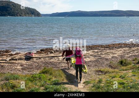 Mann und Frau tragen ihr Kajak zum Strand am Ufer von Pittwater in Palm Beach, Sydney, NSW, Australien Stockfoto