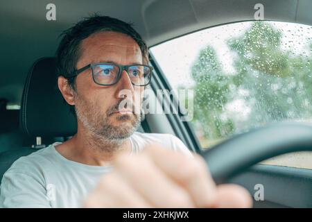 Autofahren mit schlechter Sehkraft, Porträt eines erwachsenen männlichen Fahrers mit einer Brille, die ein Lenkrad hält, selektiver Fokus Stockfoto