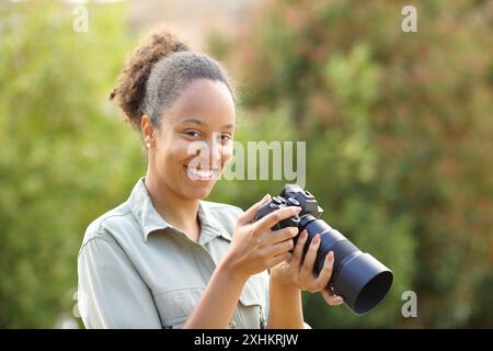 Glücklicher schwarzer Fotograf schaut in einem Park in die Kamera Stockfoto