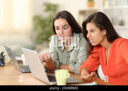 Zwei verärgerte Tele-Mitarbeiter, die zu Hause auf dem Laptop seltsame Inhalte überprüfen Stockfoto