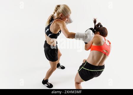 Zwei Frauen, die sich in einem intensiven Boxkampf befinden, zeigen Stärke und Beweglichkeit, konkurrieren mit Fokus und Intensität isoliert auf weißem Hintergrund Stockfoto