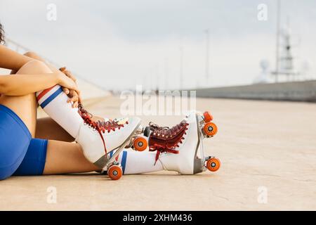 Nahaufnahme zweier Frauenbeine, die auf dem Boden sitzen, Rollschuhe und bunte Socken tragen, eine Pause machen und die Umgebung im Freien genießen. Stockfoto