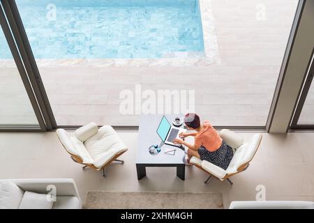 Glückliche arbeitende ältere digitale Nomadin, die mit Laptop in einer luxuriösen Pool-Villa in der Nähe des Strandes in Phuket, Thailand, sitzt. Stockfoto