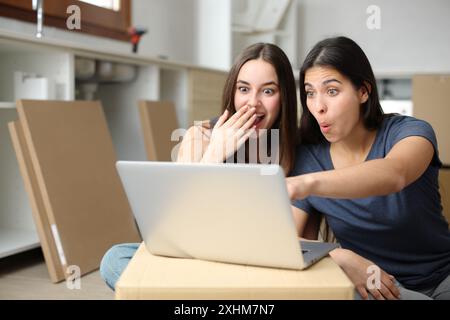 Verblüffte Mitbewohner, die den Laptop überprüfen, überraschende Nachrichten, die das Haus reformieren Stockfoto