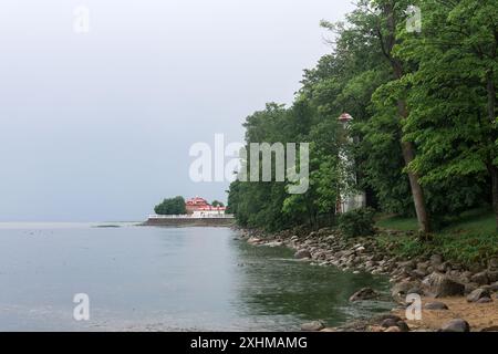 Alter Leuchtturm am Meer zwischen Bäumen vor dem Hintergrund von alten Gebäuden und Böschungen Stockfoto