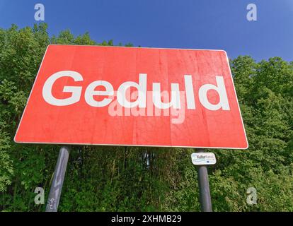 Großes Schild mit dem deutschen Wort Geduld. Roter Hintergrund mit weißer Schrift. Stockfoto