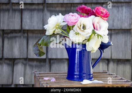 Buntes Blumenstrauß in einer blauen Kanne auf einer Holzkiste Stockfoto