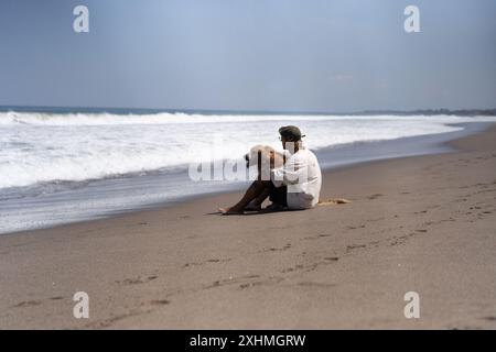 Der Mann sitzt am Meer am Strand mit goldenem Retriever-Hund. Stockfoto