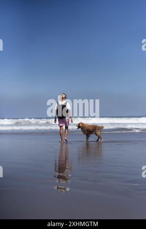 Eine Frau läuft mit ihrem goldenen Retriever-Hund am Strand entlang. Stockfoto